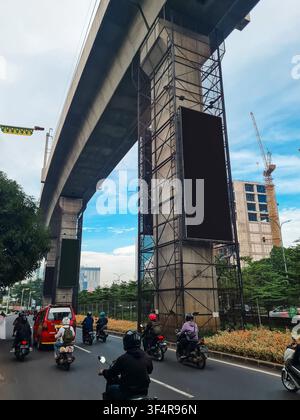 Large vertical black digital billboard on a concrete transit pillar above a busy city street with traffic. Ideal for urban advertising mockups. Stock Photo