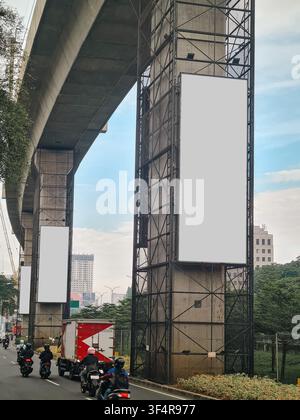 Three vertical blank white billboards mounted on metal scaffolding of elevated highway pillars. Road with traffic and city skyline in background. Idea Stock Photo
