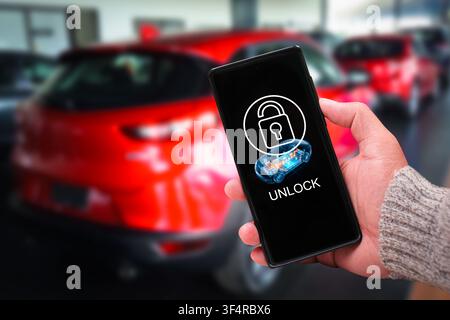 Hand holding a smartphone using a smart digital key application to unlock a modern red car remotely Stock Photo