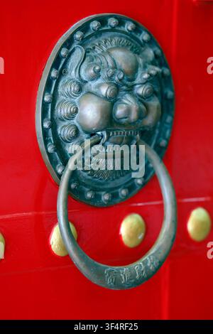 Wat Mangkon Kamalawat, or the Temple of the Dragon and Lotus. A door handle adorned with a bronze lion's head, mounted on a red door typical of Chines Stock Photo