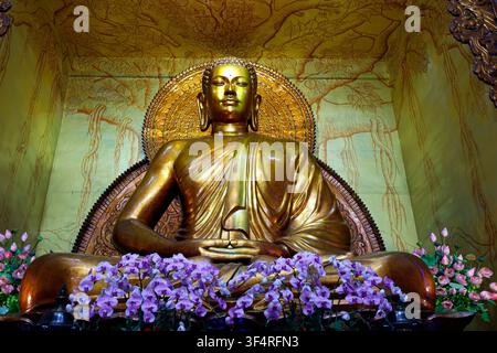 Xa Loi Pagoda. A golden statue of Buddha in meditation, adorned with orchid flowers. Ho Chi Minh City. Vietnam. Stock Photo