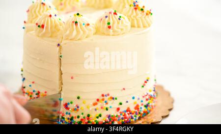 Cutting into sprinkle cake with frosting swirls Stock Photo
