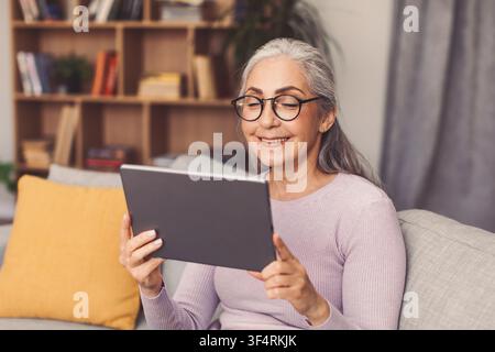 Happy Elderly Caucasian Woman Using Tablet, Smiling At Home, Technology Concept Stock Photo