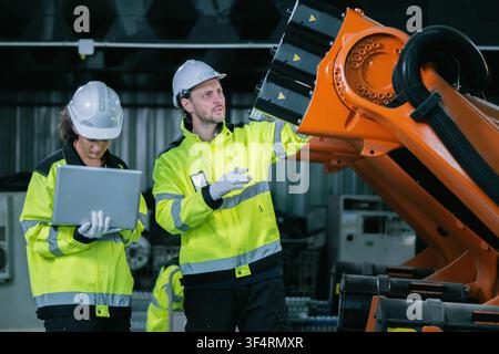 Industrial engineers team holding digital laptop inspecting parts of automated machinery factory floor. Concept of digital transformation, modern ware Stock Photo