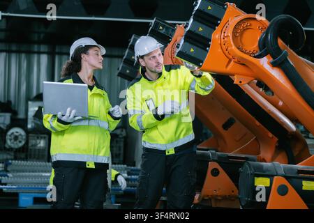 Industrial engineers team inspecting orange robotic arm automated machinery stock in warehouse factory floor. Industrial maintenance service, equipmen Stock Photo