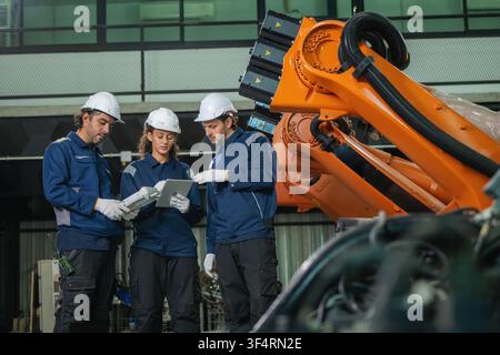 Diverse industrial engineers team holding tablet inspecting orange robotic arm smart factory. Concept of manufacturing automation system, robotics pro Stock Photo