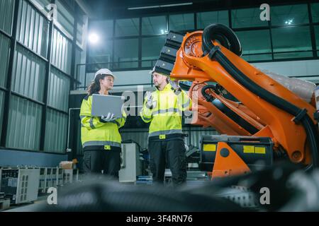 Industrial engineers inspects orange robotic arm automated machinery in warehouse factories. Concept industrial maintenance service, equipment quality Stock Photo