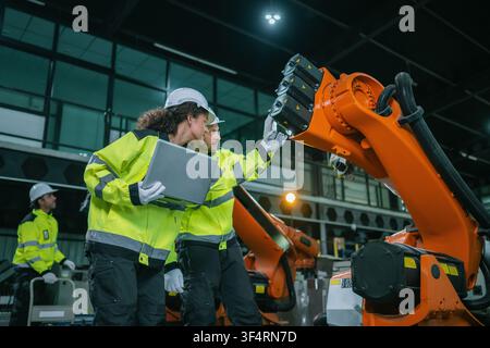 Industrial engineers team inspecting orange robotic arm automated machinery stock in warehouse factory floor. Industrial maintenance service, equipmen Stock Photo
