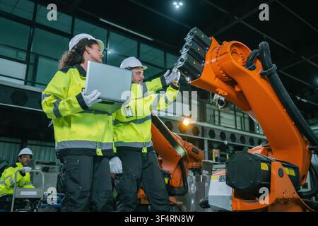 Industrial engineers inspects orange robotic arm automated machinery in warehouse factories. Concept industrial maintenance service, equipment quality Stock Photo