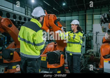 Female engineer talking explaining orange robotic arm operation male colleague holding tablet smart factory. Concept of smart factory automation syste Stock Photo