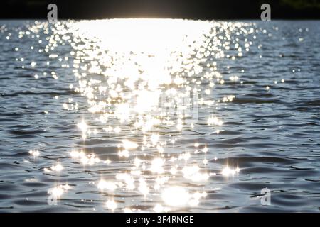 Blazing light floods the lake horizon and scatters into sparkling points across dark rippled water A vivid summer scene filled with motion and reflect Stock Photo