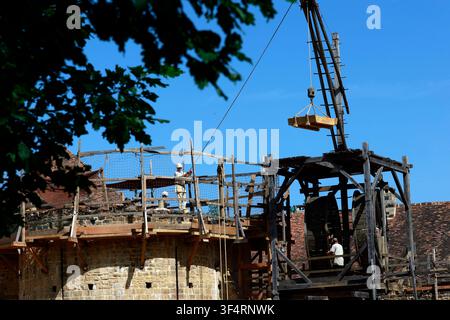 The medieval castle of Guédelon under construction, with a wooden crane lifting a load. Workers on the scaffolding. Treigny, France. Stock Photo