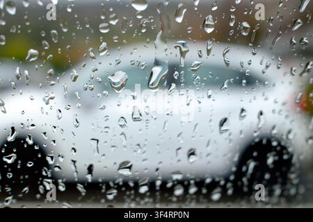 Raindrops on a window, obscuring a vehicle in the blurred background. Stock Photo