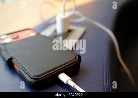 A smartphone is charging via a white charger connected to its port. The device is resting on a blue surface, ready to use. Stock Photo