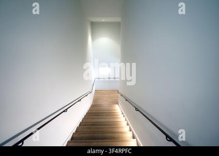 An interior staircase with wooden steps and metal handrails, illuminated by lights. Stock Photo