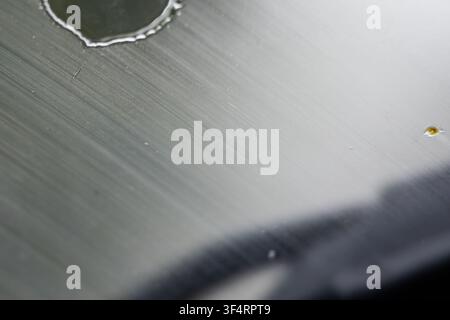 Minimal macro of a curved droplet on brushed metal beside a small golden speck. Gentle blur and line grain produce a calm technical texture with elega Stock Photo