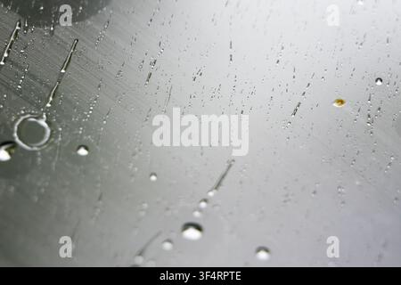 Raindrops align with faint diagonal scratches on a sleek metallic sheet. The scene blends order and randomness evoking precision industry and the beau Stock Photo