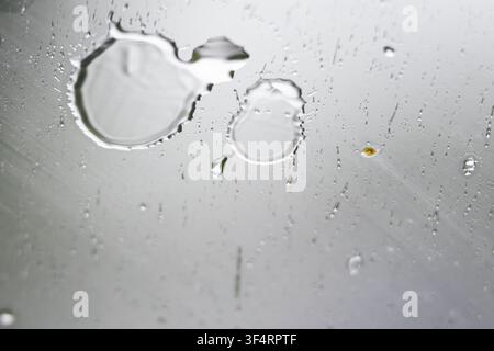 Macro view of rain droplets on smooth glass. Fine streaks slide downward as gravity works. Soft gray light fills the scene creating a calm abstract mo Stock Photo