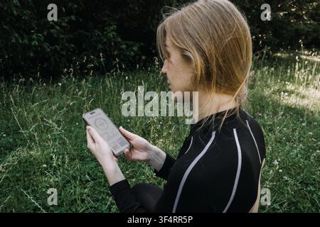 Woman sits in grassy field looking at smartphone screen with health tracking interface. FemTech app tracking, menstrual AI cycle app, women health Stock Photo