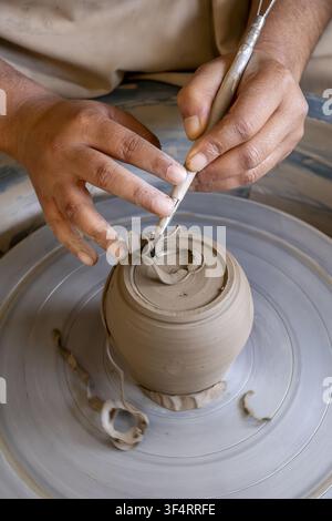 Andreta, Himachal Pradesh, India. A craftsman carefully shapes a clay object on a potter's wheel, using a specialized tool to refine its form. Stock Photo