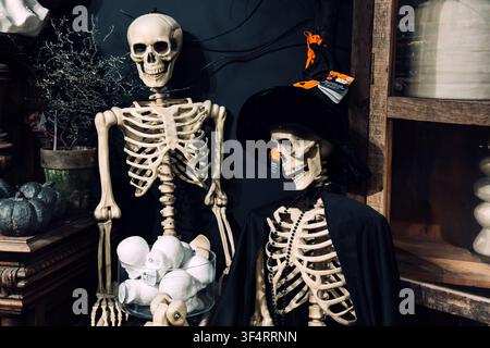 Two skeletal figures are displayed with Halloween decorations. Skeletal figures, costume party props, macabre art, Halloween display, retail Stock Photo