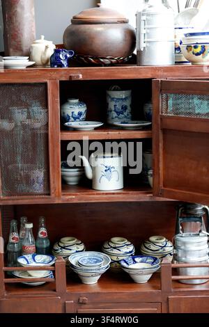 A dark wooden cabinet displays a collection of traditional blue-and-white ceramic tableware. Bowls, plates, and teapots are neatly arranged on the she Stock Photo