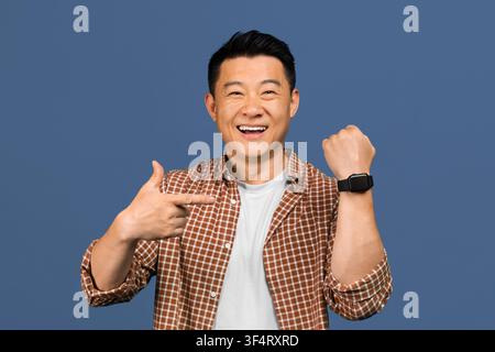 Happy Asian Man Showing Smartwatch On Wrist, Smiling, Studio Background, Technology Concept Stock Photo