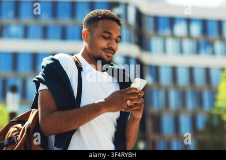 Young African American Man Using Smartphone Outdoors, Relaxed Posture, Urban Setting Stock Photo