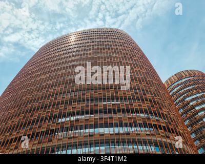Low angle view of contemporary circular office towers featuring distinctive orange horizontal louvers against a bright sky, representing modern urban Stock Photo
