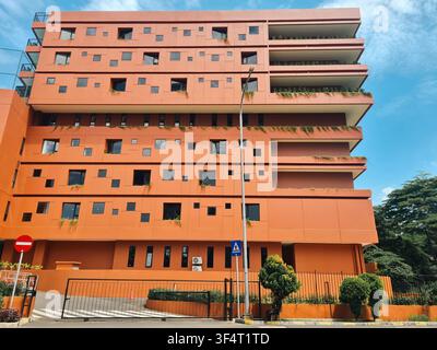 Exterior view of a contemporary orange building featuring irregular square windows and green vegetation on balconies against a clear sky. Stock Photo