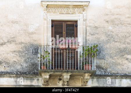 Ornate stone balcony with closed brown shutters & potted plants, enhancing the building's historic facade, Ragusa Ibla,  Sicily, Italy. Stock Photo