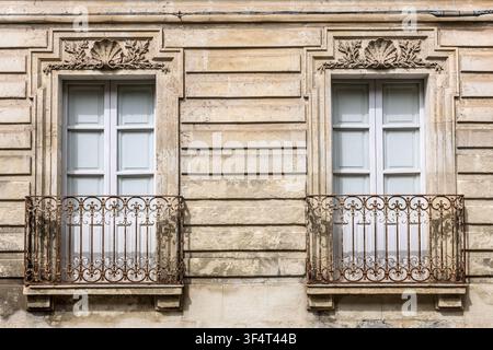 2 ornate windows with closed shutters & rusty metal balconies, Noto, Sicily, Italy Stock Photo