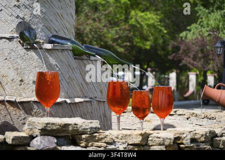 Red glasses under a wine fountain, flowing from bottles across stone, in sunshine, fountain with wine bottles filling glasses, Milestii Mici Winery, M Stock Photo