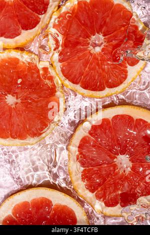 Juicy citrus fruit pattern with ruby red grapefruit slices under splashing water. Stock Photo