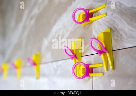 Tile leveling system with yellow wedges, pink clips used for precise ceramic porcelain tile installation, ensuring flat surface, preventing lippage, m Stock Photo