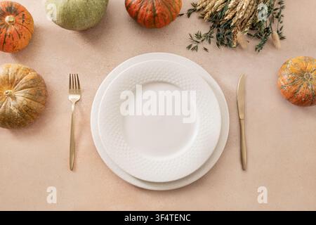 Elegant autumn table setting with sage green plate, linen napkin, white decorative pumpkin, dried grasses and golden cutlery on beige background with Stock Photo