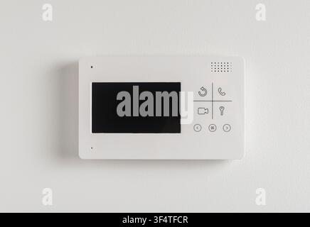 A video intercom panel with a small screen and buttons is mounted on a light textured wall. The doorphone device allows residents to view and communic Stock Photo