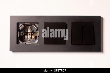 Black double electrical socket and switch frame mounted cleanly on a white wall. The modern black panel shows a double outlet and switch combination. Stock Photo