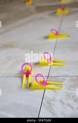 Tile leveling system with yellow wedges, pink clips used for precise ceramic porcelain tile installation, ensuring flat surface, preventing lippage, m Stock Photo