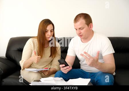 Couple reviewing financial documents and using mobile phone for online banking and budgeting Stock Photo