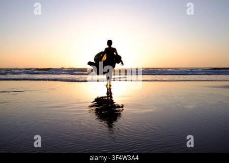 Woman walking on a beach during sunset, her silhouette and reflection highlighting freedom and serenity Stock Photo