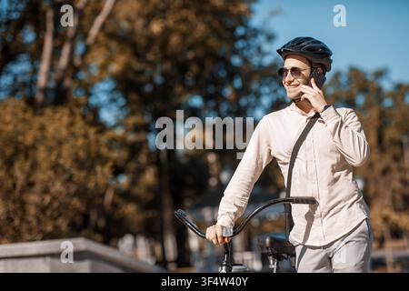 Safe bike ride. Smiling guy in helmet speaks by smartphone Stock Photo