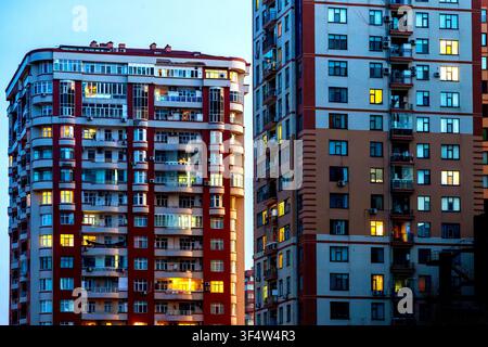 Close-up of two illuminated residential high-rise facades with balconies and air conditioning units at dusk. Baku, Azerbaijan. Stock Photo