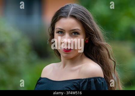A woman with long hair and red lips poses confidently in an outdoor area. Stock Photo