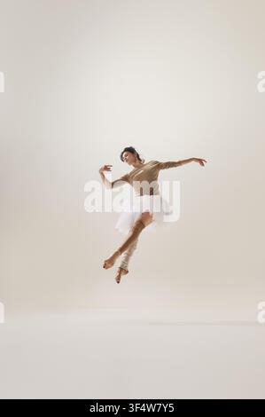 Ballerina performing energetic airborne jump with open arms on neutral studio background Stock Photo