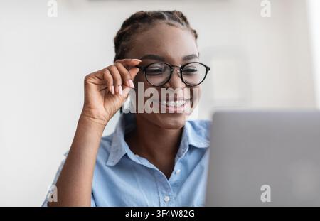 Young Specialist. African lady with eyeglasses and braces using laptop in office Stock Photo