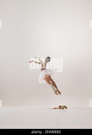 Athletic ballerina performing airborne leap above pointe shoes on clean white background Stock Photo