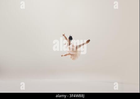 Dynamic ballerina captured in extended airborne split leap against white background Stock Photo
