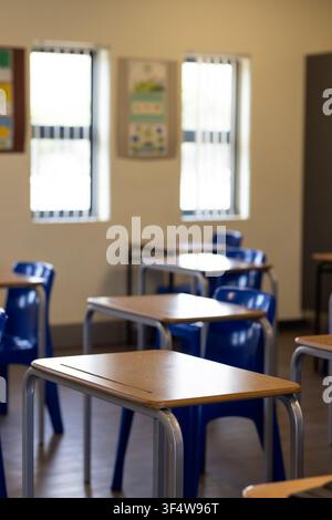Single wooden student desk is sitting at center in classroom with blue chair tucked, blinds visible Stock Photo