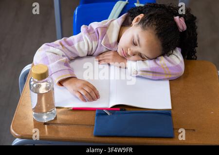 African American child sleeping head resting on notebook in class, blue pouch, in plaid jacket Stock Photo